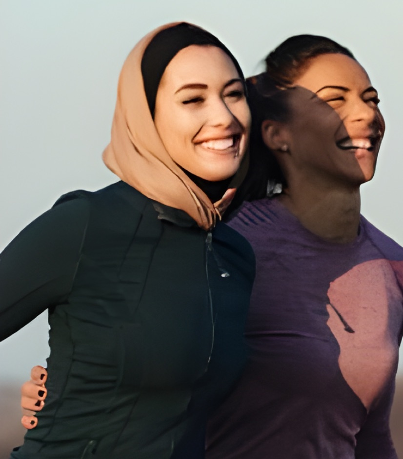 Two smiling women running together outdoors, one in a hijab